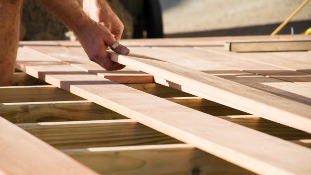 Man placing a plank of wood in a deck home renovation on a warm sunny day